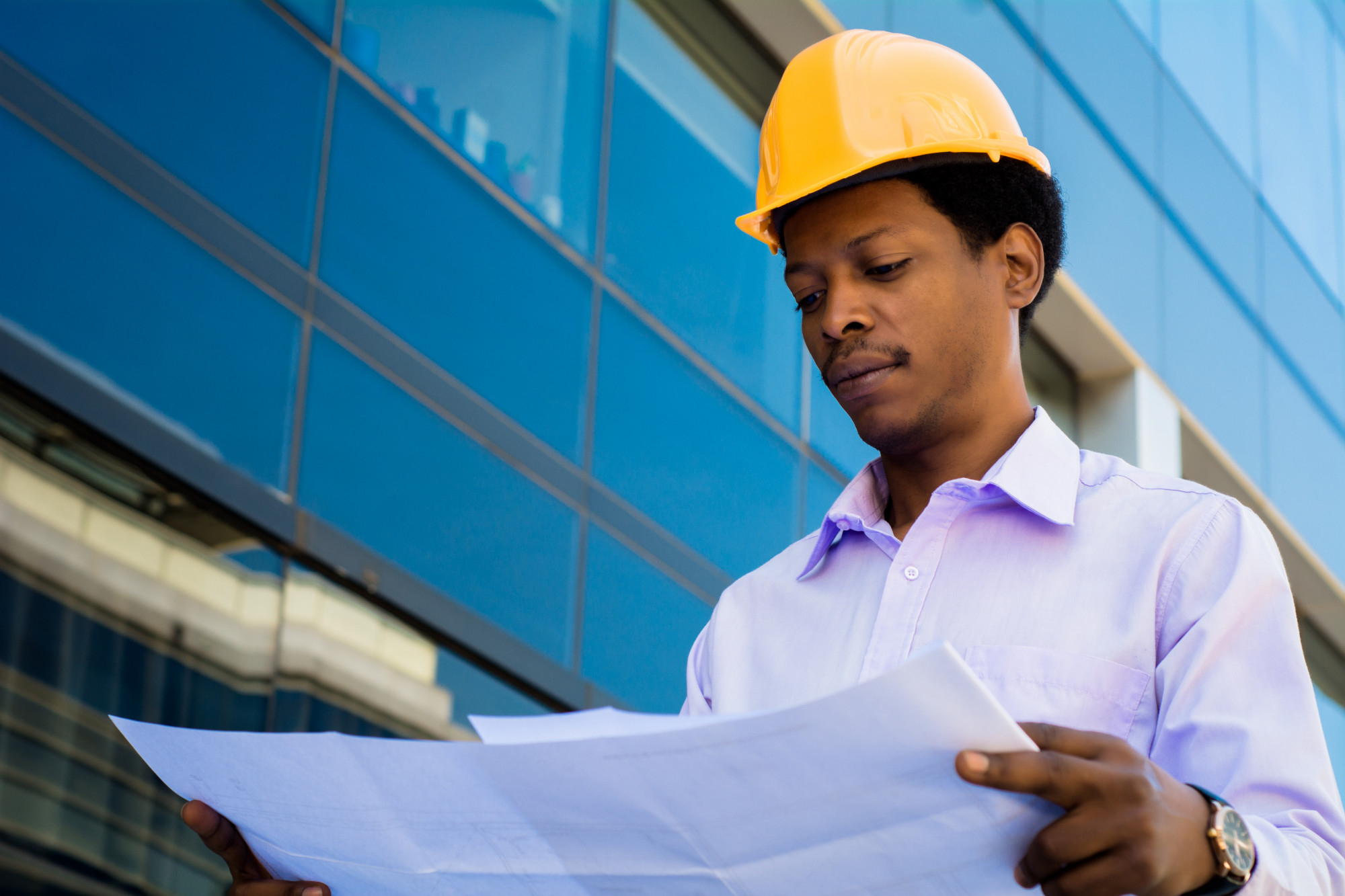 portrait of professional architect in helmet looking at blue prints outside modern building engineer and architect concept